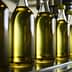 Row of glass bottles filled with olive oil on a production line in a factory setting. - Olive Oil Times