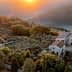 Aerial view of a rustic farmhouse surrounded by olive trees and hills during sunset. - Olive Oil Times