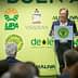 A speaker presenting at an olive oil industry event with a green backdrop featuring various logos. - Olive Oil Times