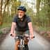 Older man wearing a helmet riding a bicycle on a forest trail during daylight. - Olive Oil Times