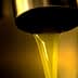 Golden olive oil flowing from a metal tap into a container in a close-up view. - Olive Oil Times