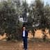 A man wearing sunglasses standing next to a large olive tree in a field. - Olive Oil Times