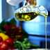 A person pouring olive oil from a glass bottle into a metal bowl in a kitchen setting. - Olive Oil Times
