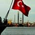 Turkish flag waving on a ship with cranes and industrial structures in the background. - Olive Oil Times