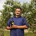 Man standing in an olive grove holding a bottle of olive oil with olive trees in the background. - Olive Oil Times