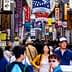 Crowd of people walking through a bustling street market filled with colorful signs in Japan. - Olive Oil Times