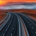 A highway winding through a mountainous landscape during sunset with orange and purple hues in the sky. - Olive Oil Times