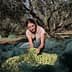 Woman holding freshly harvested olives while sitting on a green net in an olive grove. - Olive Oil Times