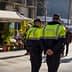 Two police officers in green and black uniforms walking in an urban area with a flower shop in the background. - Olive Oil Times