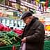 An elderly man examining vegetables in a grocery store with green produce bins. - Olive Oil Times