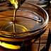 Golden olive oil being poured into a glass bowl placed on a wooden surface. - Olive Oil Times