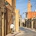 Narrow street lined with brick buildings in a village, with a person walking along the side. - Olive Oil Times