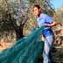 Woman in a blue shirt pulling a green net used for olive harvesting in an olive grove. - Olive Oil Times