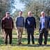 Six men standing together in an olive grove, dressed in casual and formal attire. - Olive Oil Times