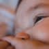Close-up view of a baby's face with a focus on the eye and hand. - Olive Oil Times
