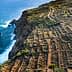 Aerial view of terraced agricultural fields along a coastal cliff with ocean waves below. - Olive Oil Times