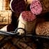 Various wine corks with different colors and markings placed in a wire basket. - Olive Oil Times