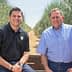 Two men sitting on a bench in an olive grove, surrounded by olive trees. - Olive Oil Times
