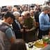 A group of people gathered around a table discussing various items at an outdoor event. - Olive Oil Times