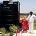 A large black water storage tank labeled 'SUPER TUFF' next to a red pump system and a man in white clothing. - Olive Oil Times