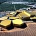 Aerial view of a modern olive oil processing facility with a hexagonal design and yellow roofs. - Olive Oil Times