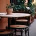 A round table with a potted plant and three chairs in a narrow outdoor setting. - Olive Oil Times