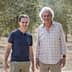 Two men standing in an olive grove, both smiling and dressed casually in light clothing. - Olive Oil Times