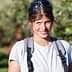 A woman with sunglasses and a backpack smiling while standing in an orchard with trees in the background. - Olive Oil Times