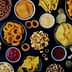 An assortment of snack foods including chips, pretzels, and popcorn arranged in bowls on a dark surface. - Olive Oil Times