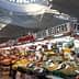 Market stall displaying a variety of fruits and vegetables under a large ceiling structure. - Olive Oil Times
