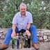 A man seated on a stone wall with various olive oil bottles displayed in front of him. - Olive Oil Times
