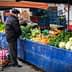 Man examining fresh vegetables at a market stall with various produce displayed. - Olive Oil Times