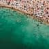 Aerial view of a crowded beach with swimmers and colorful umbrellas along the shoreline. - Olive Oil Times