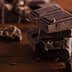Several pieces of dark chocolate stacked on a wooden surface with additional chocolate fragments scattered around. - Olive Oil Times