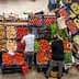 Two individuals arranging fresh vegetables and fruits at a market stall with various produce. - Olive Oil Times