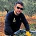 Man wearing sunglasses and gloves sorting olive leaves in a container in an olive grove. - Olive Oil Times