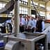 Group of individuals observing an oil extraction machine during a demonstration in a factory setting. - Olive Oil Times