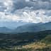 A panoramic view of mountains under a cloudy sky with varying shades of green vegetation. - Olive Oil Times