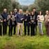 Group of twelve individuals standing in an olive grove, each holding a bottle of olive oil. - Olive Oil Times