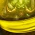 Close-up of a jar containing green liquid with a demon illustration visible inside. - Olive Oil Times