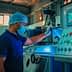 A worker in a blue shirt and hairnet operating a control panel in an industrial environment. - Olive Oil Times