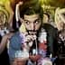 Man sipping a cocktail through a straw while surrounded by people at a party. - Olive Oil Times