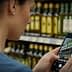 A woman photographing olive oil bottles on a shelf using a smartphone in a store. - Olive Oil Times