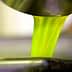 Bright green olive oil pouring from a metal container into a bowl. - Olive Oil Times