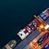 Aerial view of container ships docked at a port with colorful shipping containers stacked on the deck. - Olive Oil Times