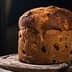 A round loaf of bread with a golden-brown crust and visible raisins on a wooden surface. - Olive Oil Times