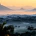 A misty landscape featuring mountains and valleys during sunrise with soft light and fog. - Olive Oil Times