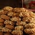 A large stack of honey-dipped cookies topped with crushed nuts on a wooden surface. - Olive Oil Times