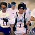 Three male runners participating in a competitive race, wearing athletic gear and numbers on their shirts. - Olive Oil Times