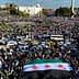 A large crowd gathered in a public square holding a Syrian flag with three stars. - Olive Oil Times